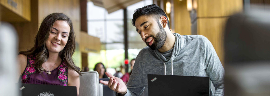 Two students smiling and workin on laptops in Bethany Hall.