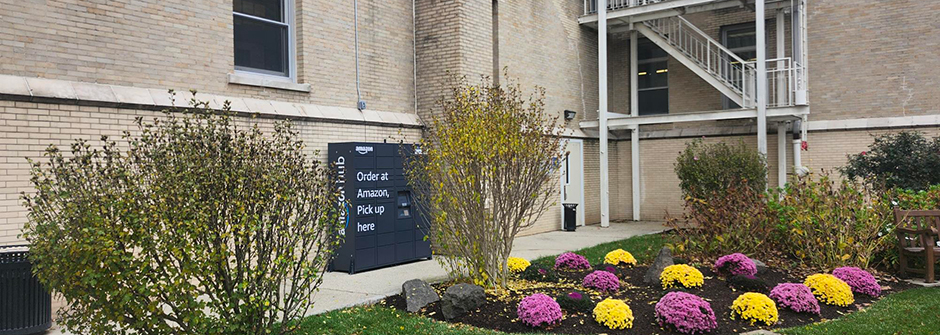 Amazon locker on campus behind Mooney Hall near some flowers 
