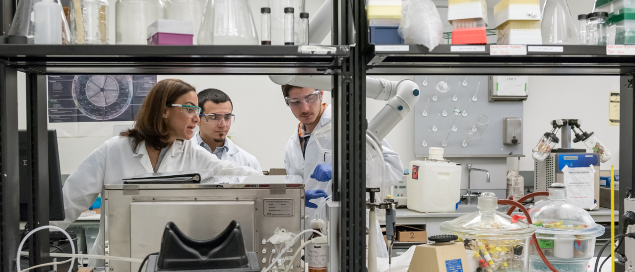 Image of three chemists or chemistry students working in a lab. 