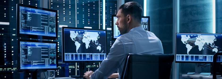 A professional working at a desk working with data on multiple monitors.