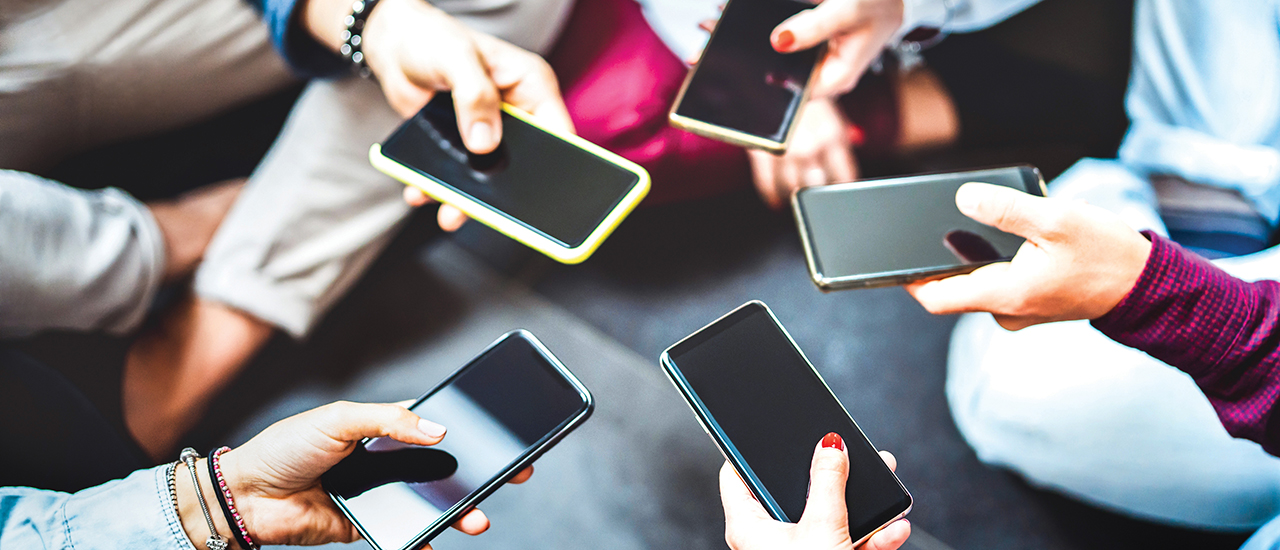 People sitting in a circle holding out their cell phones.