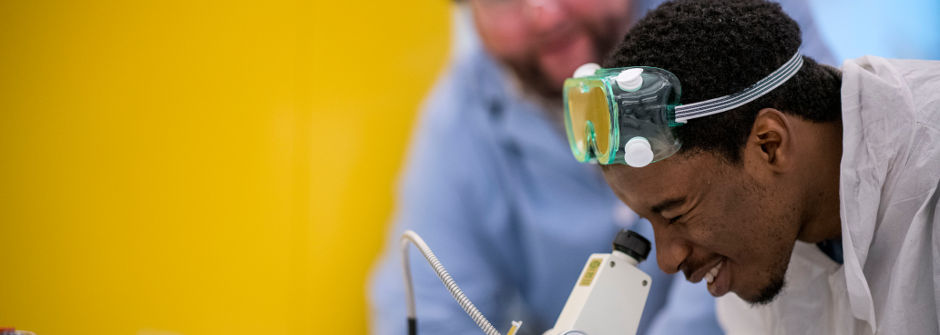 Student looking through a microscope with a faculty member overseeing the lab experiment. 