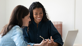 Two women working over a laptop smiling. 