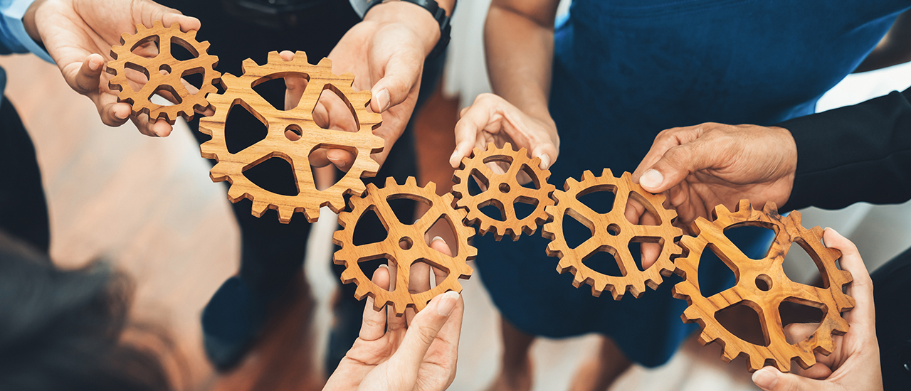 People holding gears working to fit them together.