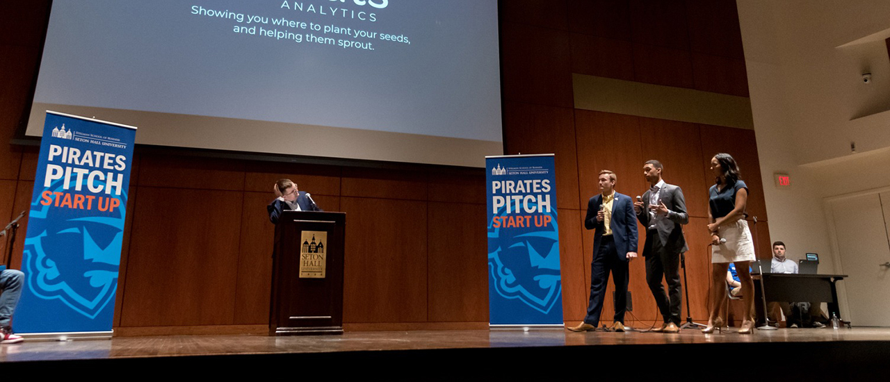 Image of a participant at a podium and three judges during Pirates Pitch. 