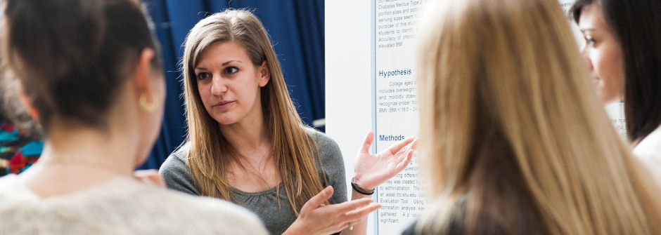 Students at Petersheim Academic Exposition presenting her poster to a group of bystanders.