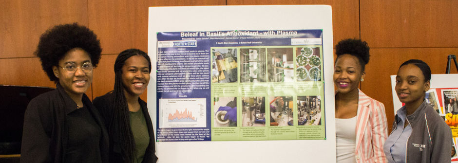 Four students standing next to poster presentation. 