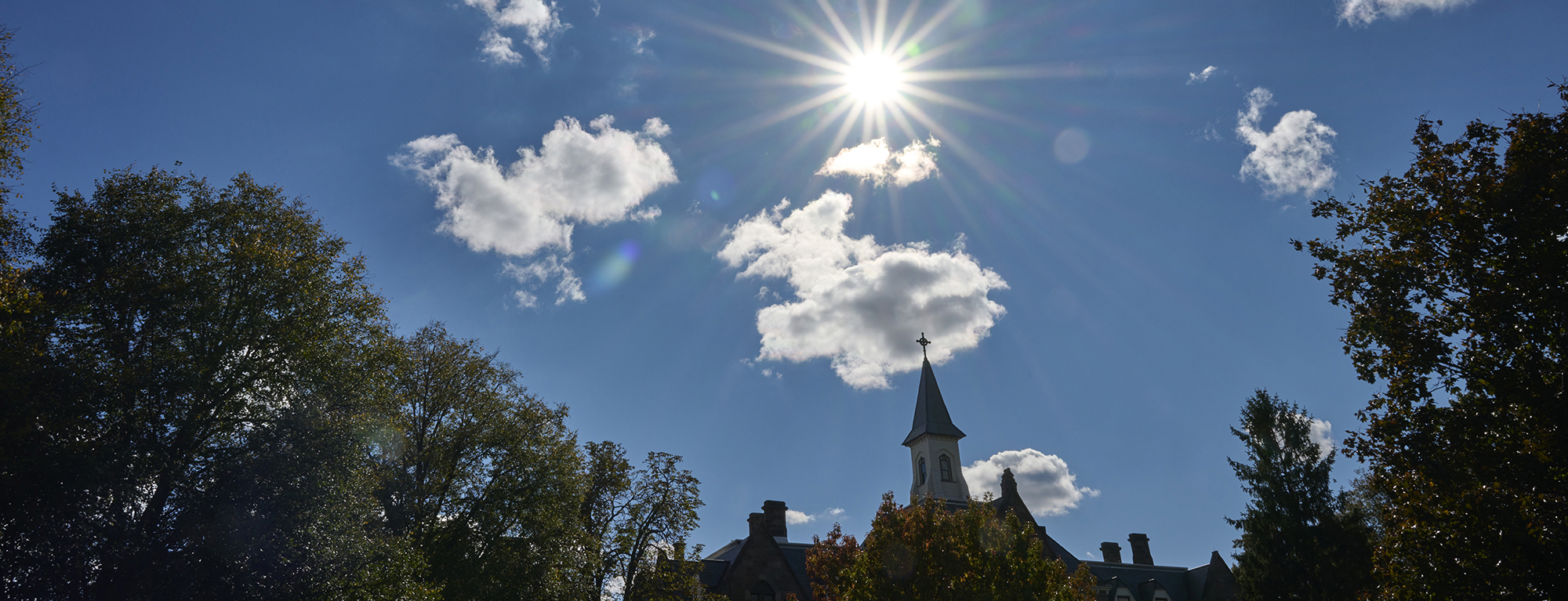 A photo of the blue sky with the sun and clouds over Presidents Hall.