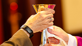 Two hands holding the chalice at communion. 