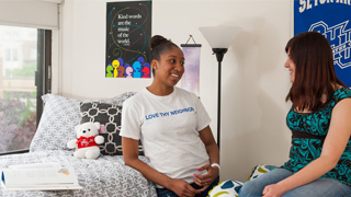 Image of two students standing in their dorm talking.